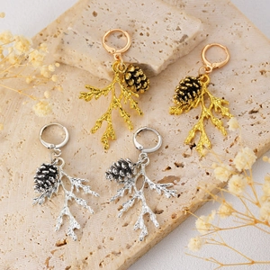Close-up of gold and silver pine cone earrings on stone texture with dry flower décor