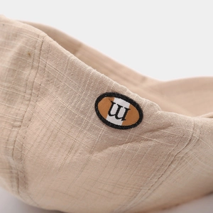 Macro detail of beige woven fabric newsboy hat featuring an oval 'm' logo patch