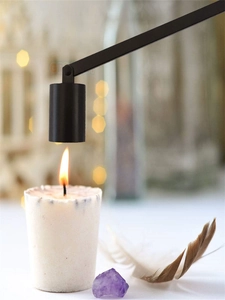 Scented candle detail shot featuring a black metal extinguisher bell hovering above a white candle.