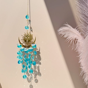 Close-up of golden sun and moon suncatcher with blue crystal beads casting light shadows
