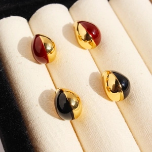 Elegant water drop stud earrings in red-gold and black-gold enamel on white velvet tray