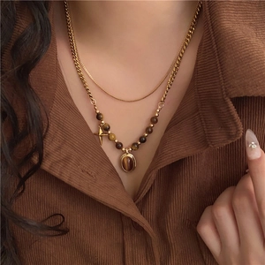 Double-layered gold necklace with tiger eye beads and oval pendant on velvet shirt
