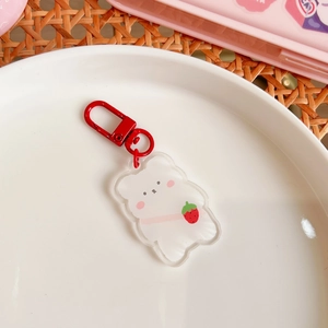Close-up of a white acrylic cartoon bear keychain with a strawberry and red metal hook