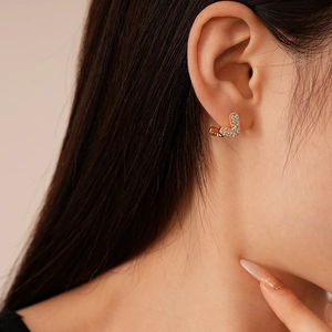 Close-up of a gold heart earring with pavé zircon stones worn by a model in warm light