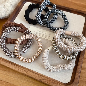 Detail of woven elastic hair ties in neutral tones displayed on a wooden tray