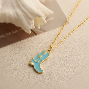 Gold chain necklace with blue cowboy boot pendant and star detail on beige fabric