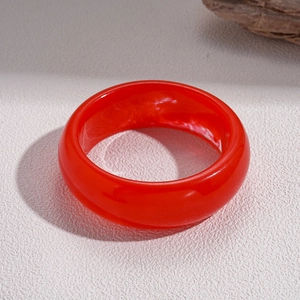 Detail of red resin chunky bangle with glossy translucent finish on a light beige background