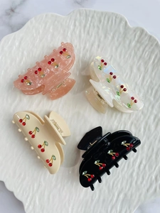 Macro shot of 4-color hair claws featuring sparkling rhinestone cherry motifs in a tray