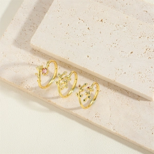 Three vintage gold leaf rings with colorful zircon accents on a beige stone surface