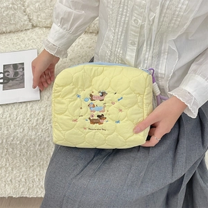 Close-up of embroidered dachshund pattern on quilted cream cosmetic bag with pastel accents