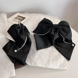 Detail showing two black satin bow hair clips with gold trim and elegant pearls