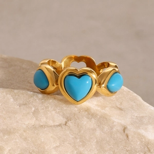 Detail of gold heart ring with turquoise stones on natural stone base for women