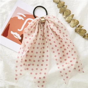 Pink polka dot bow hair tie with gold ring detail on a white linen artistic background