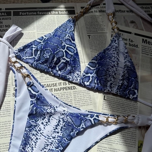 Détail du bikini imprimé serpent bleu avec chaînes dorées décoratives sur fond de journal