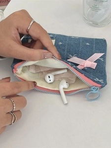 Portamonete in denim con fiocco rosa ricamato e chiusura a zip tenuto in mano