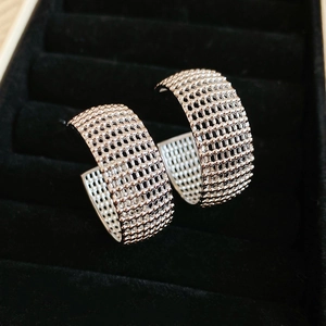 Macro detail of silver C-shaped mesh earrings with intricate hollow woven metal texture