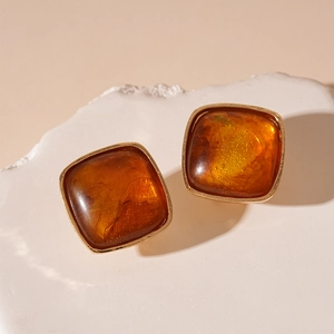 Close-up of square amber resin earrings with golden metal frame on white stone