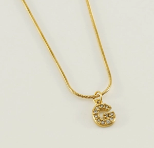 Close-up of gold snake chain necklace featuring a zircon-encrusted letter G pendant