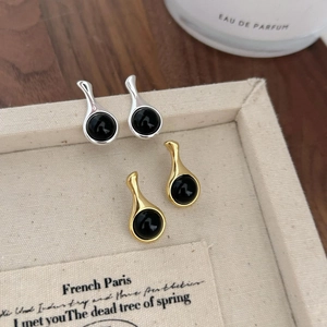 Detailed close-up of teardrop onyx stud earrings in gold and silver on a jewelry box