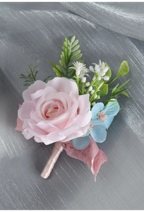 Close-up of a handmade pink rose boutonniere with satin ribbon and blue floral accents