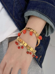Close-up of golden link bracelets featuring red strawberry and cherry charms worn on wrist