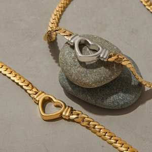 Detailed view of bicolor heart-shaped clasps on flat snake chains over grey stones