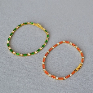 Macro detail of gold-plated bracelets featuring green and orange rectangular zircons