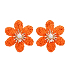 Detail of hand-woven orange raffia flower earrings with white pearl and rhinestones