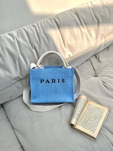 Detailed shot of a blue woven straw tote bag with Paris print and beige canvas straps