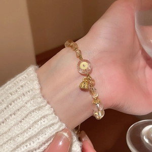 Macro shot of citrine beads and gold lotus charm bracelet on woman's wrist