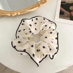 Close-up of cream scrunchie with black floral pattern and ruffled edges on a desk