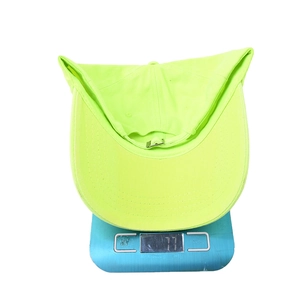 Detail view of a neon yellow baseball cap on a scale showing a lightweight 77g weight