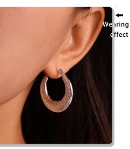 Close-up of silver U-shaped hoop earring with textured scale pattern on model