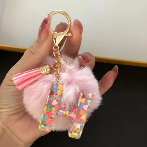 Close-up of pink pompom and resin letter H keychain with colorful heart sequins