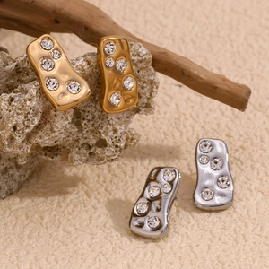 Macro detail of geometric gold and silver earrings with zircons on natural textured props