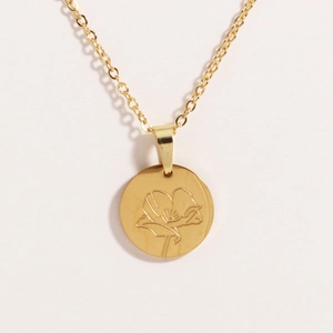 Macro detail of oval gold titanium steel pendant featuring a delicate floral rose engraving