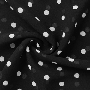 Gros plan sur un tissu mousseline noir à pois blancs avec un drapé en spirale élégant et léger