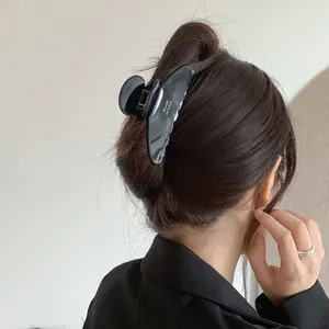 Glossy black acetate hair claw clip with French lettering shown on model's hair