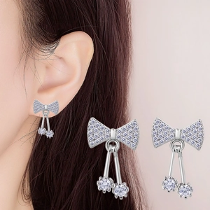 Macro shot of silver bow stud earrings with sparkling white zircons on model ear