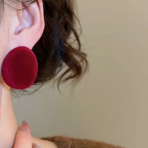 Gros plan d'une boucle d'oreille ovale en velours bordeaux portée par un mannequin
