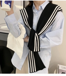 Detail of a soft knit scarf with black and white stripes worn as a shoulder wrap accessory