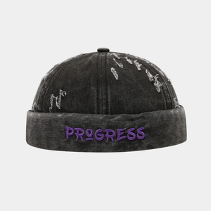 Détail du bonnet miki en denim délavé noir avec broderie PROGRESS violette et trous usés