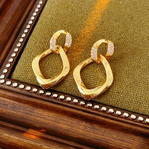 Dettaglio di orecchini dorati a forma ovale intrecciata con pavé di zirconi luminosi