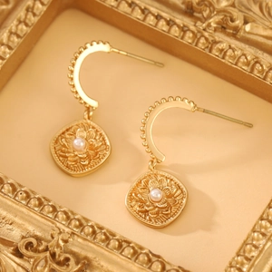 Macro detail of golden fan earrings featuring floral relief and small white pearls