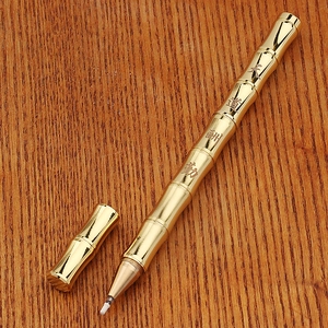 Detail of vintage brass bamboo pen with gold finish and engraved calligraphy on wood surface