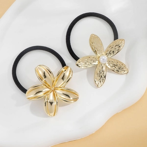 Close-up of golden metal flower hair ties with pearl center on ceramic display plate