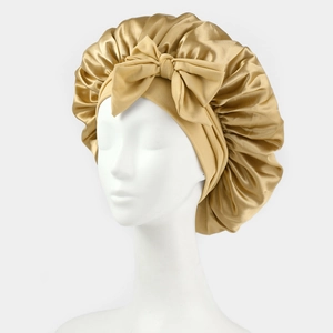 Detail of golden satin sleep bonnet featuring a large decorative bow and elastic band