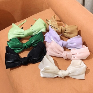 Elegant satin bow headbands in various candy colors shown on a soft orange cushion