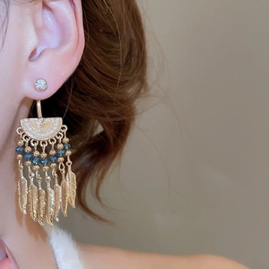 Detailed close-up of retro gold tassel earrings with blue beads and feather pendants