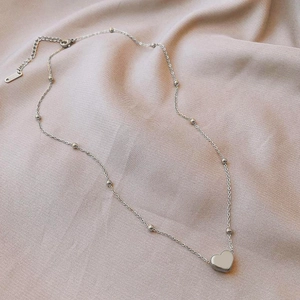 Detailed view of silver heart pendant on a beaded chain over pink silk fabric
